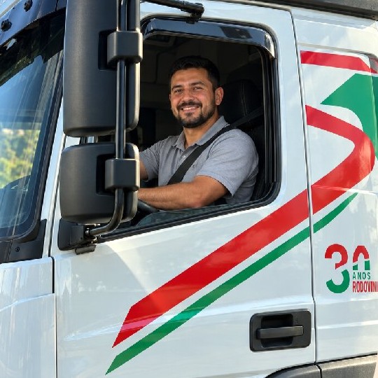 Motorista da Rodovini ao lado de um caminhão vermelho